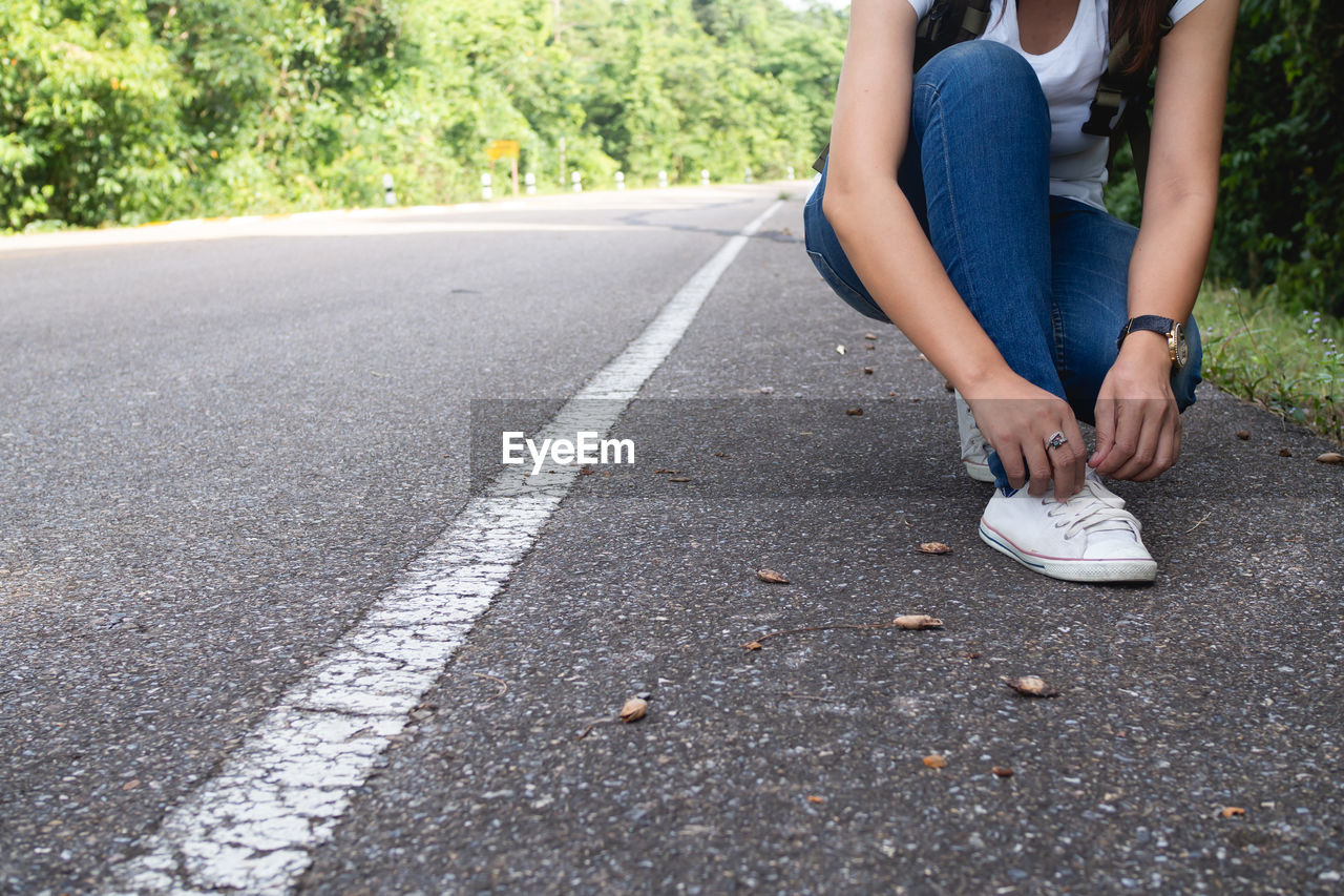 Low section of woman tying shoelace on road