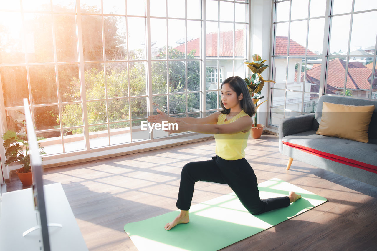 Young woman praticing yoga over television at home