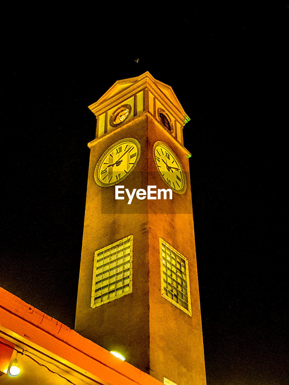 LOW ANGLE VIEW OF CLOCK TOWER AGAINST BUILDING IN CITY AT NIGHT