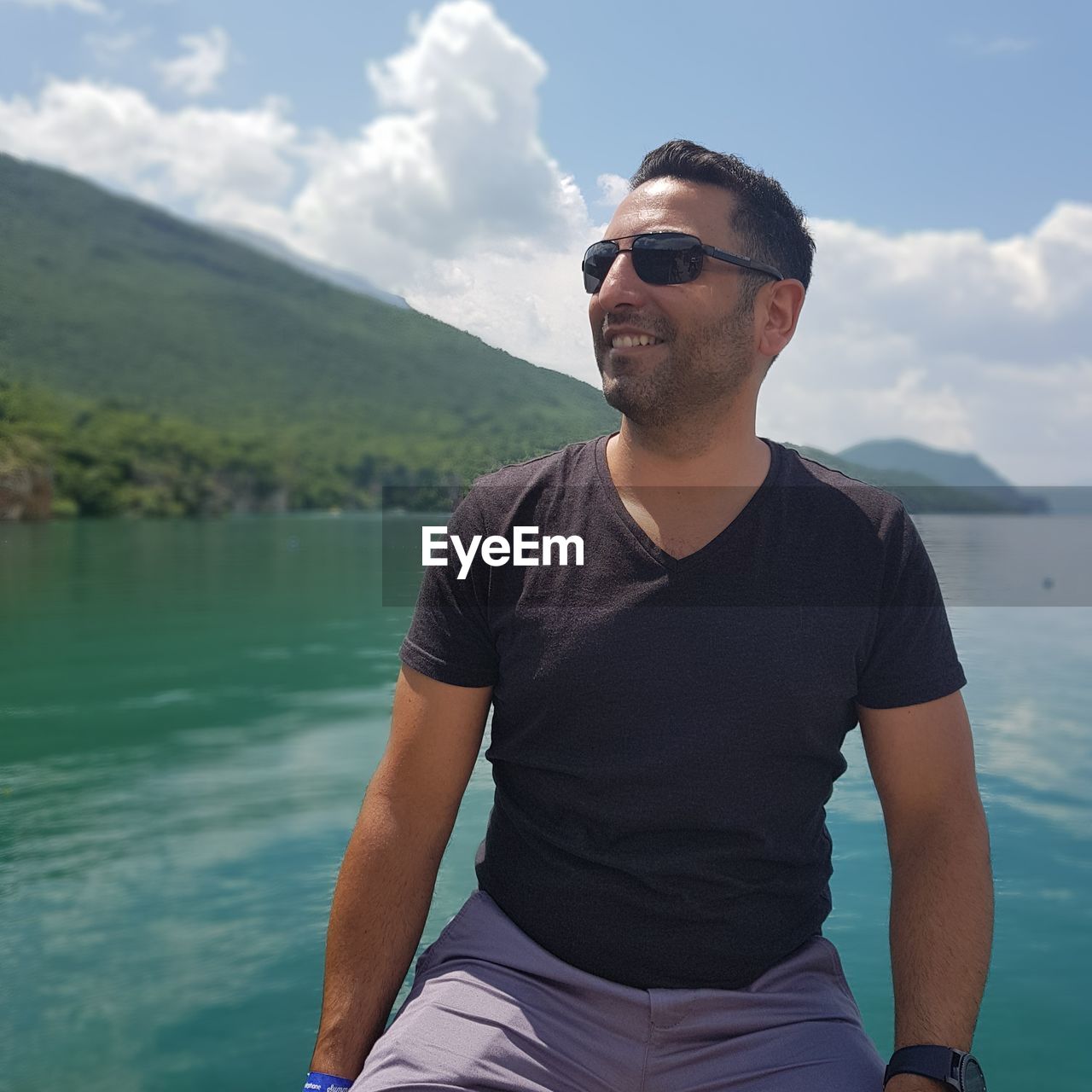 Mid adult man wearing sunglasses at lake against mountain