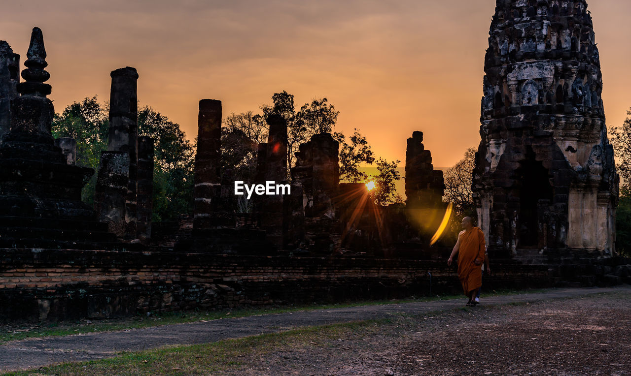 Monk walking at historic temple against sky during sunset