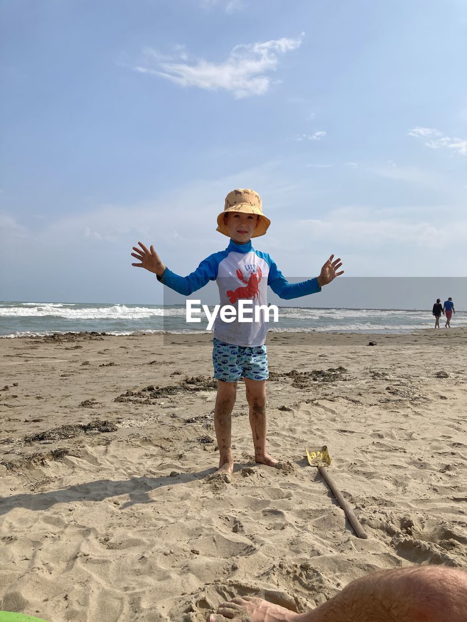 Rear view of boy with arms outstretched standing at beach against sky