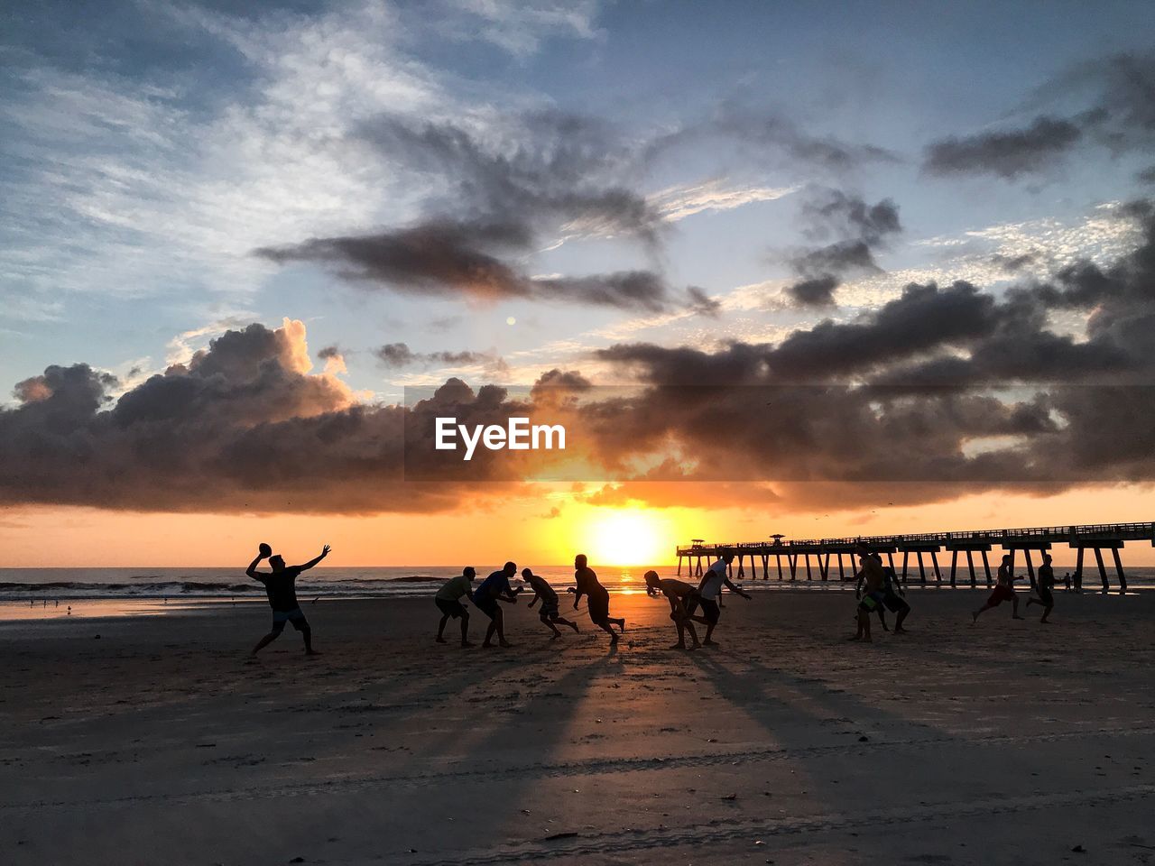 People playing on sand against sea during sunset