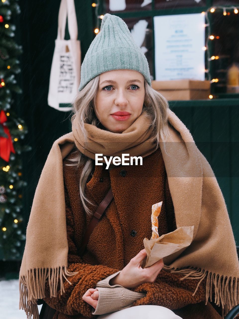 Young woman with blonde hair wearing brown fur coat eating sweet food on the christmas market.