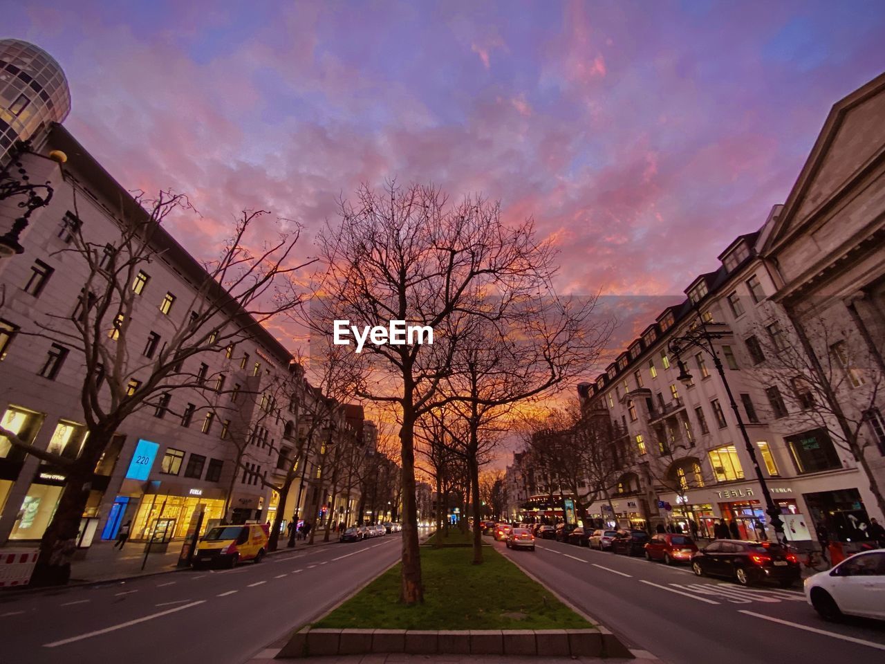 STREET AMIDST BUILDINGS AGAINST SKY AT SUNSET