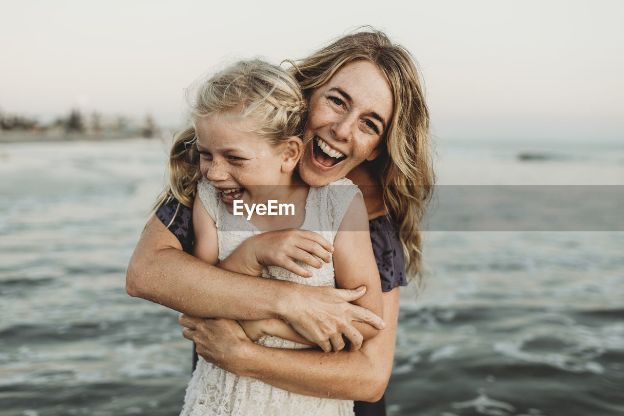 Mother embracing young girl with freckles in ocean laughing