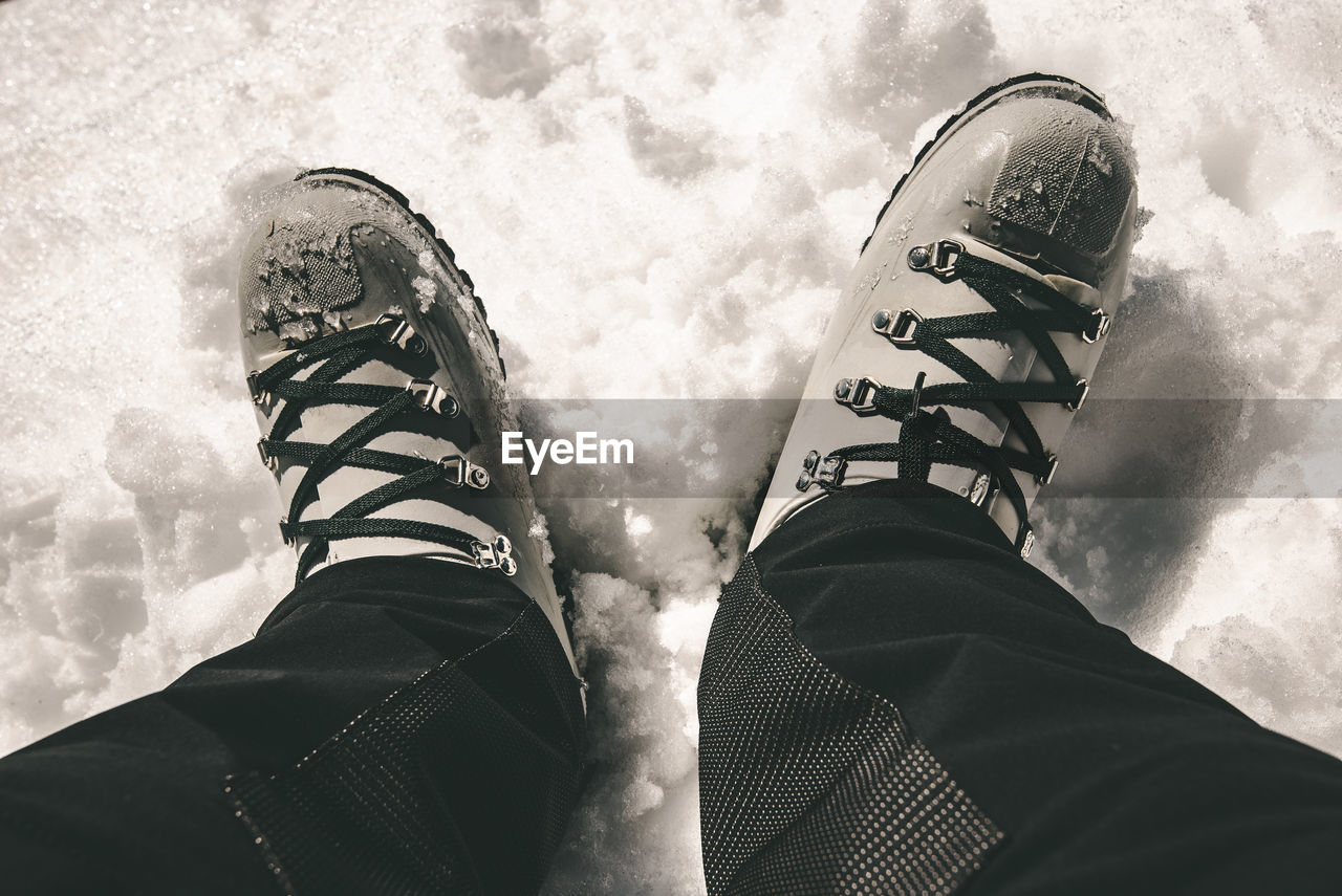 LOW SECTION OF PERSON STANDING BY SHOES AGAINST SKY