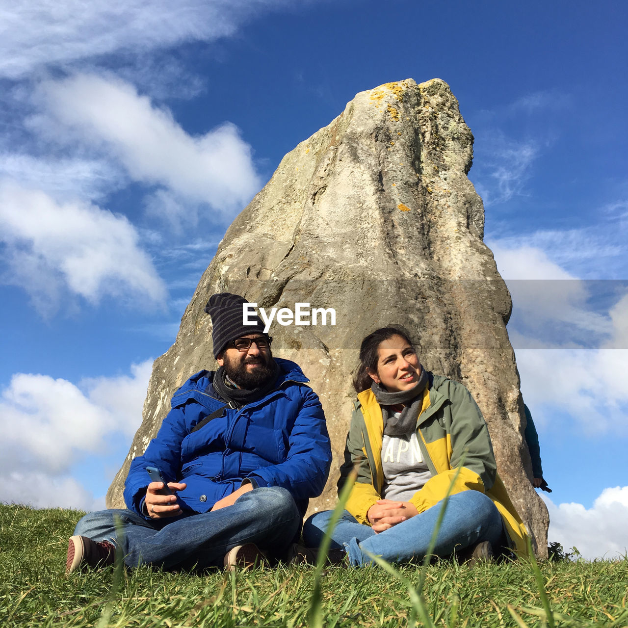 Couple sitting on grassy field against sky at avebury stone circle