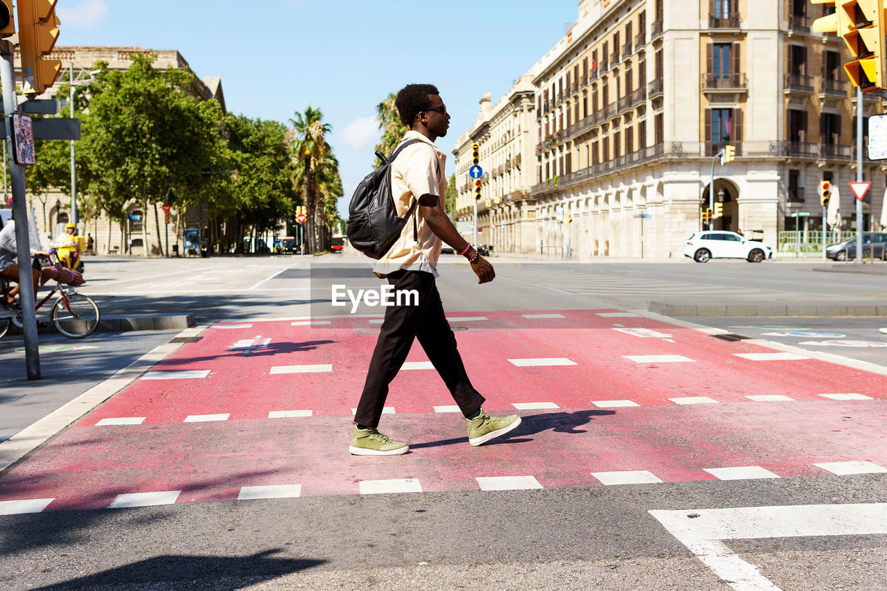 Side view of ethnic male in casual wear crossing asphalt road on sunny day in barcelona