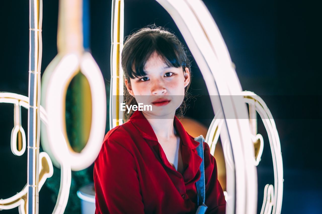 Portrait of young woman by illuminated lighting equipment at night