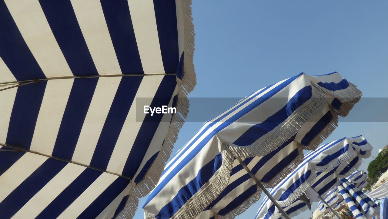 Low angle view of striped beach umbrellas against clear sky