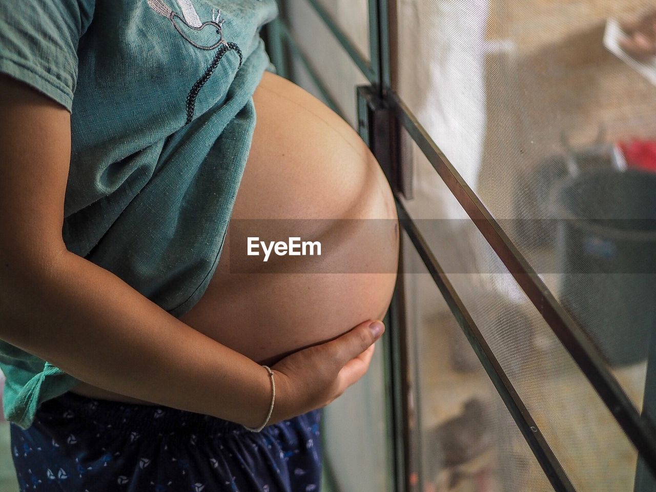 Midsection of pregnant woman standing by window