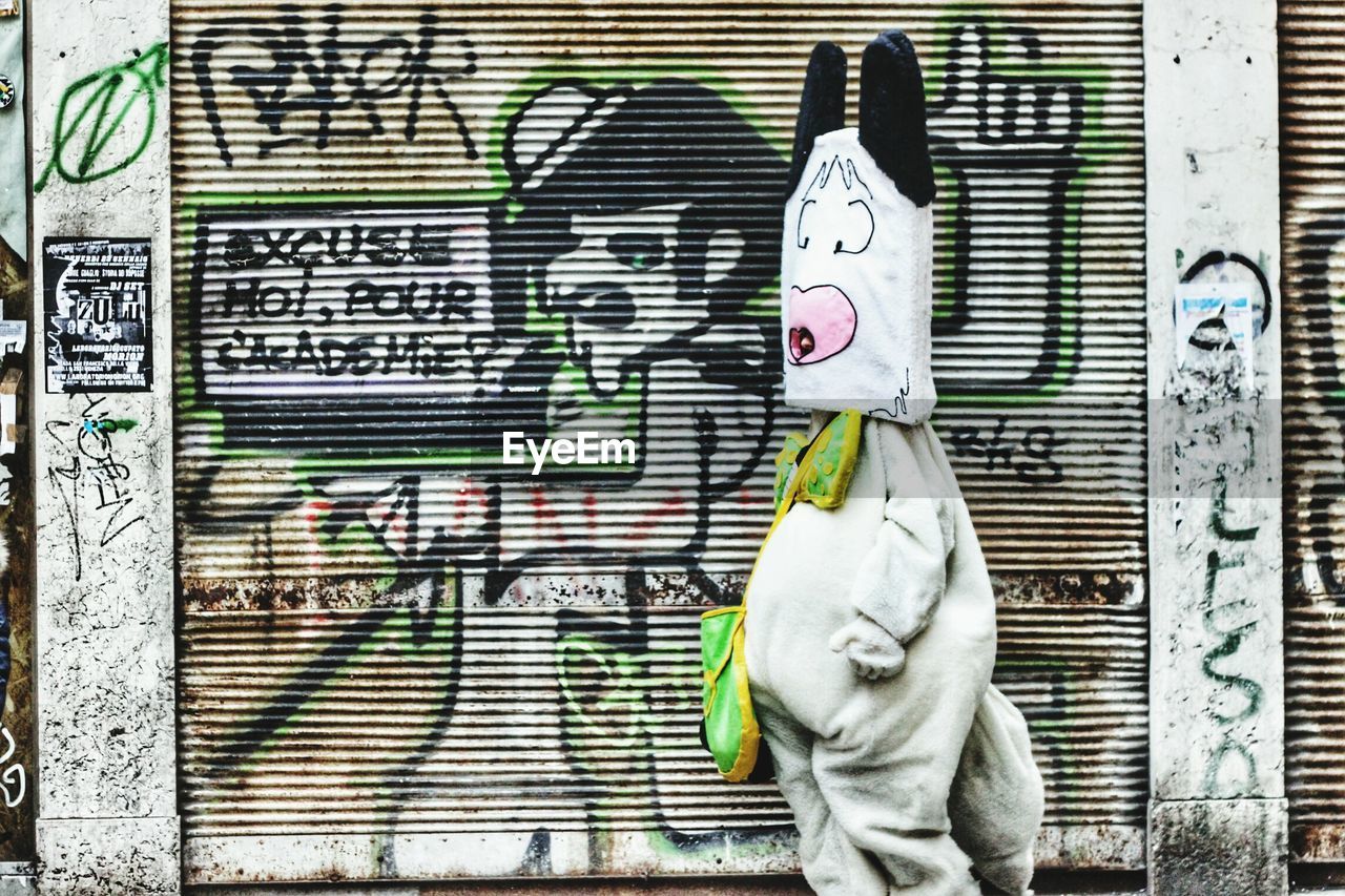 Person wearing costume standing against shutter with graffiti