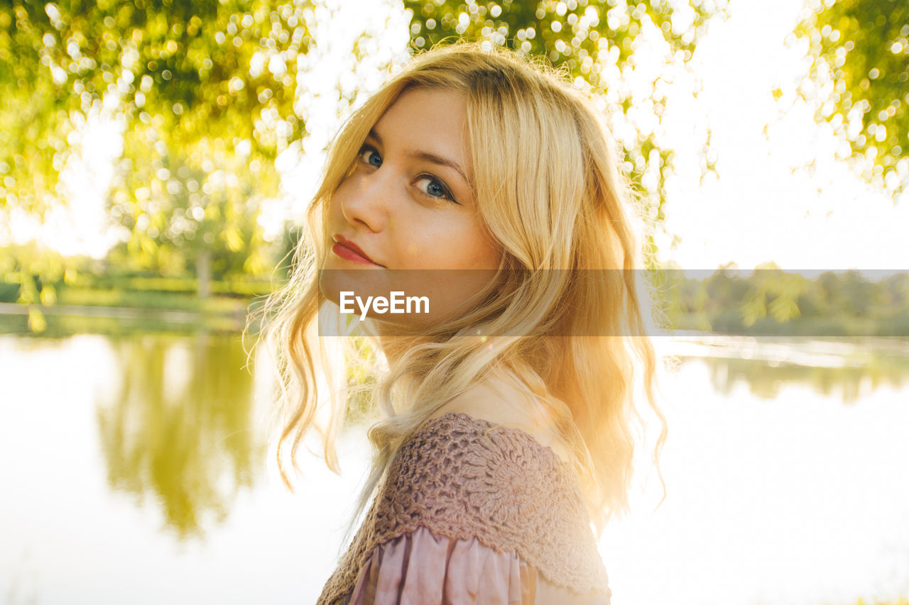 Portrait of young woman standing against lake