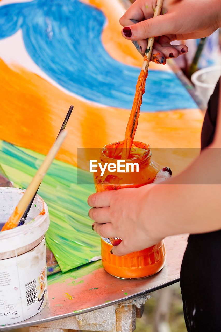 Midsection of woman with orange paint in container