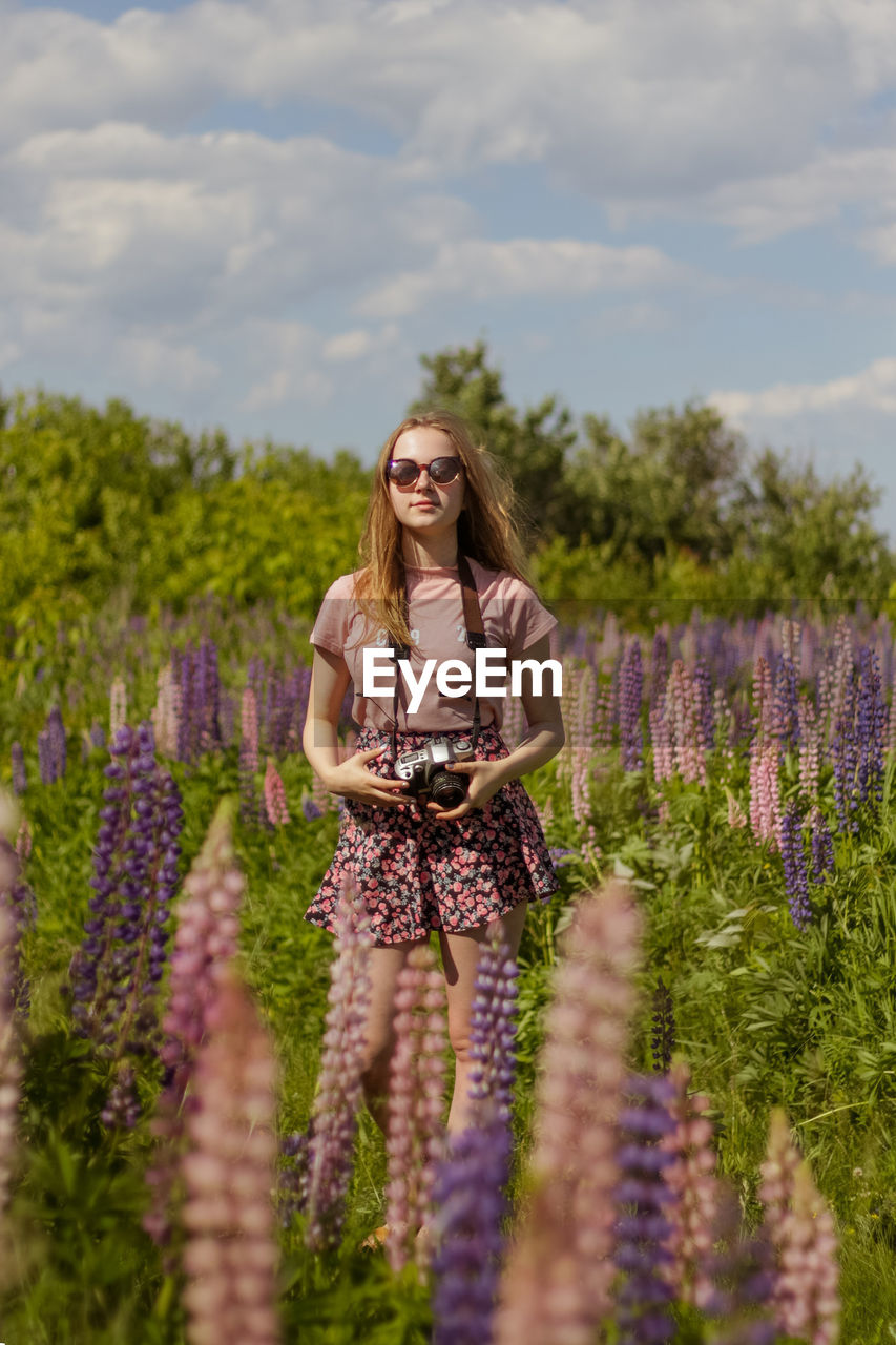 Beautiful young woman in the field of lupins with photo camera