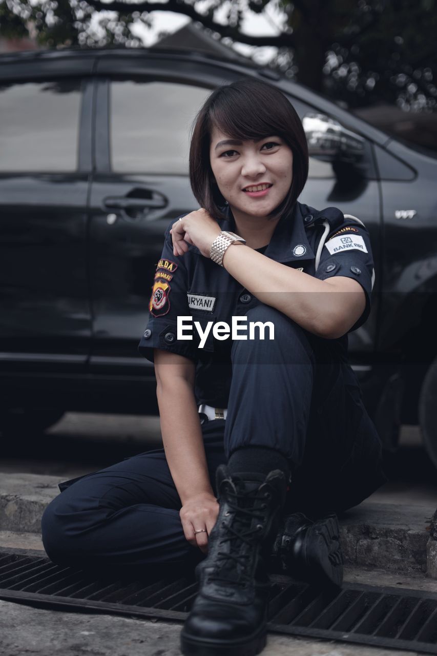 Portrait of female police in uniform sitting against car