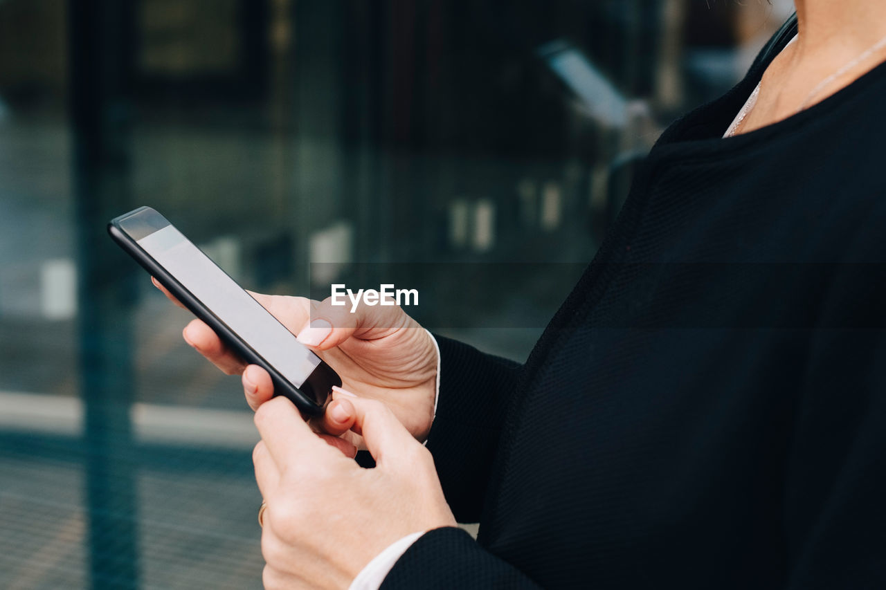 Midsection of businesswoman using smart phone while standing in city