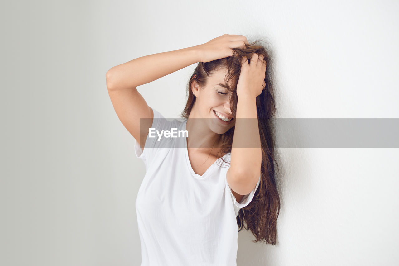 Smiling young woman with hand in hair against white wall