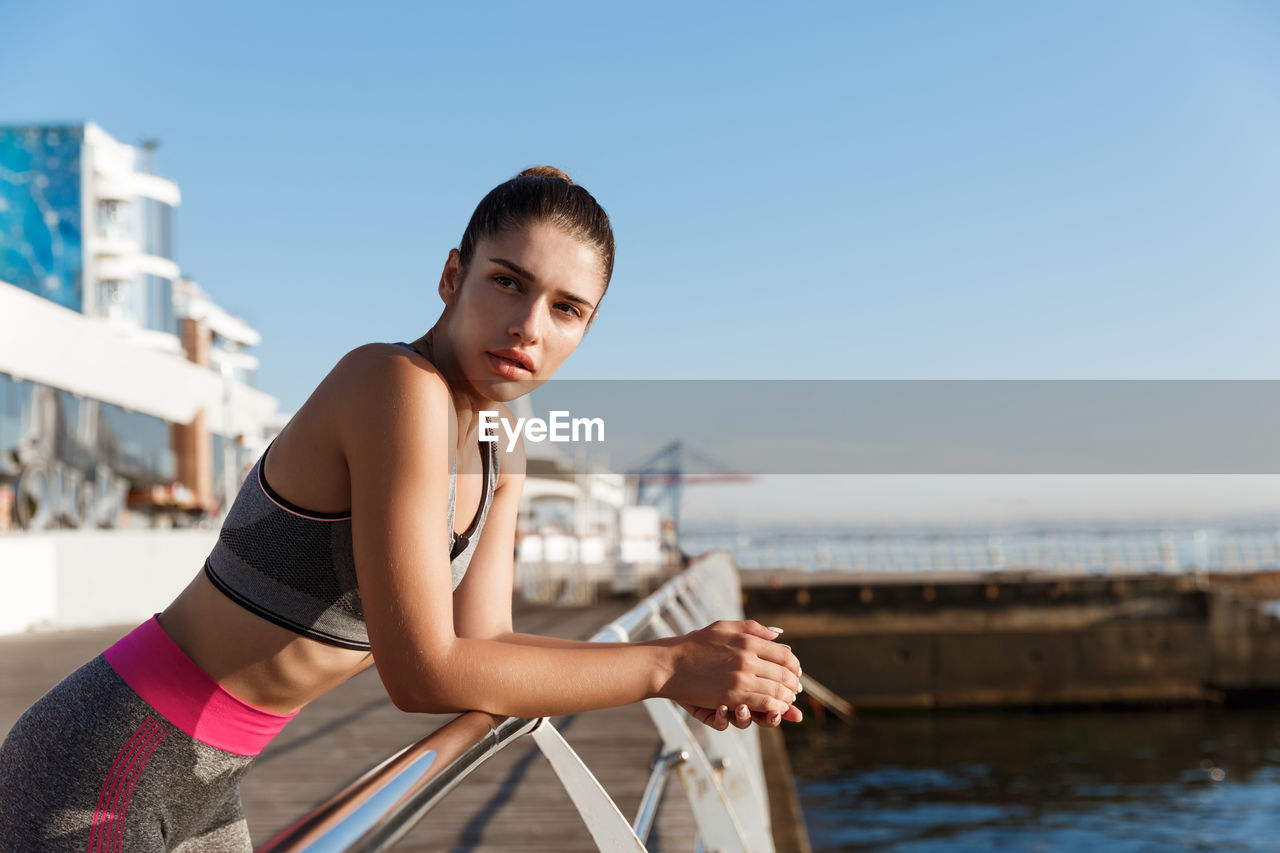 Woman looking away while leaning on railing against sky