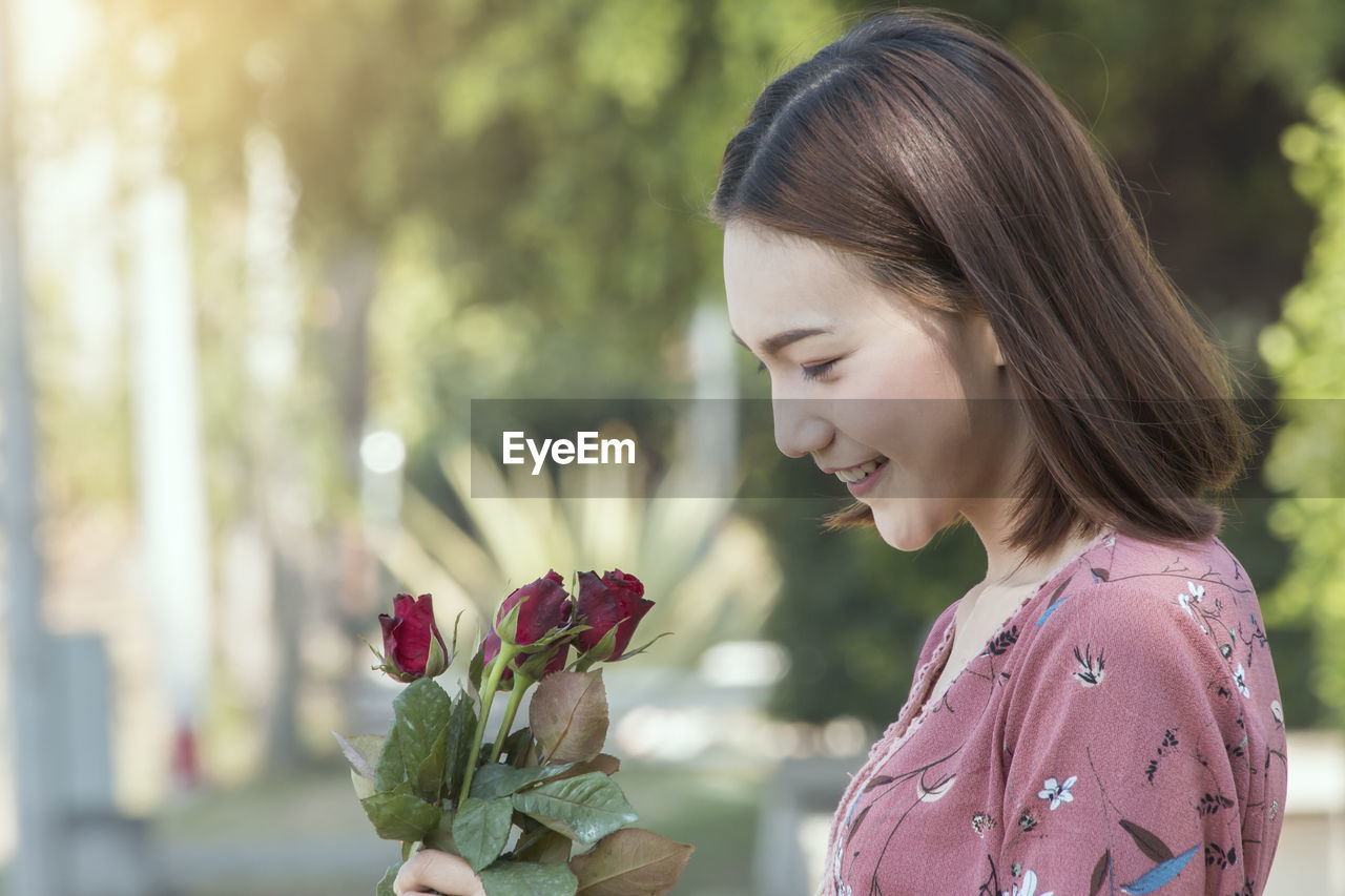 Close-up of smiling woman looking at red roses