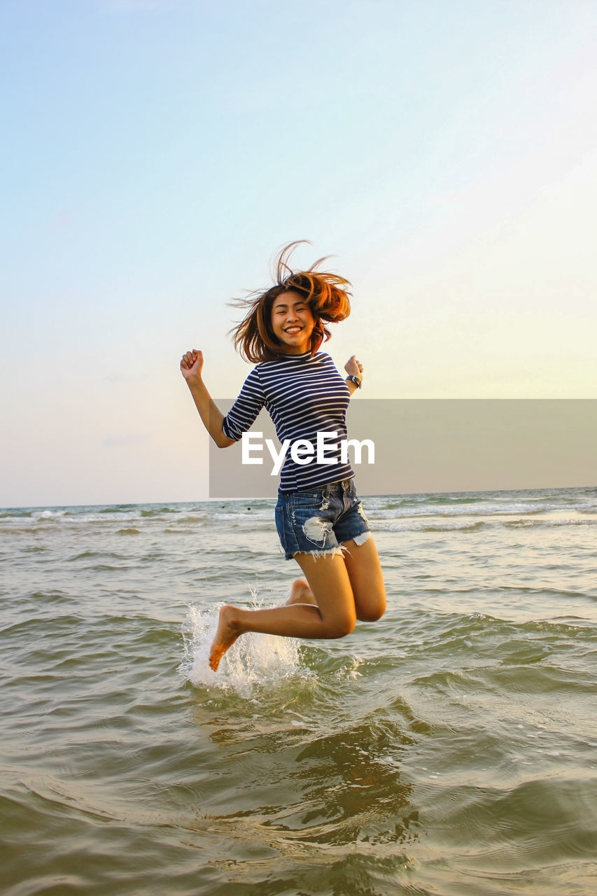 Full length of happy woman jumping in sea against sky