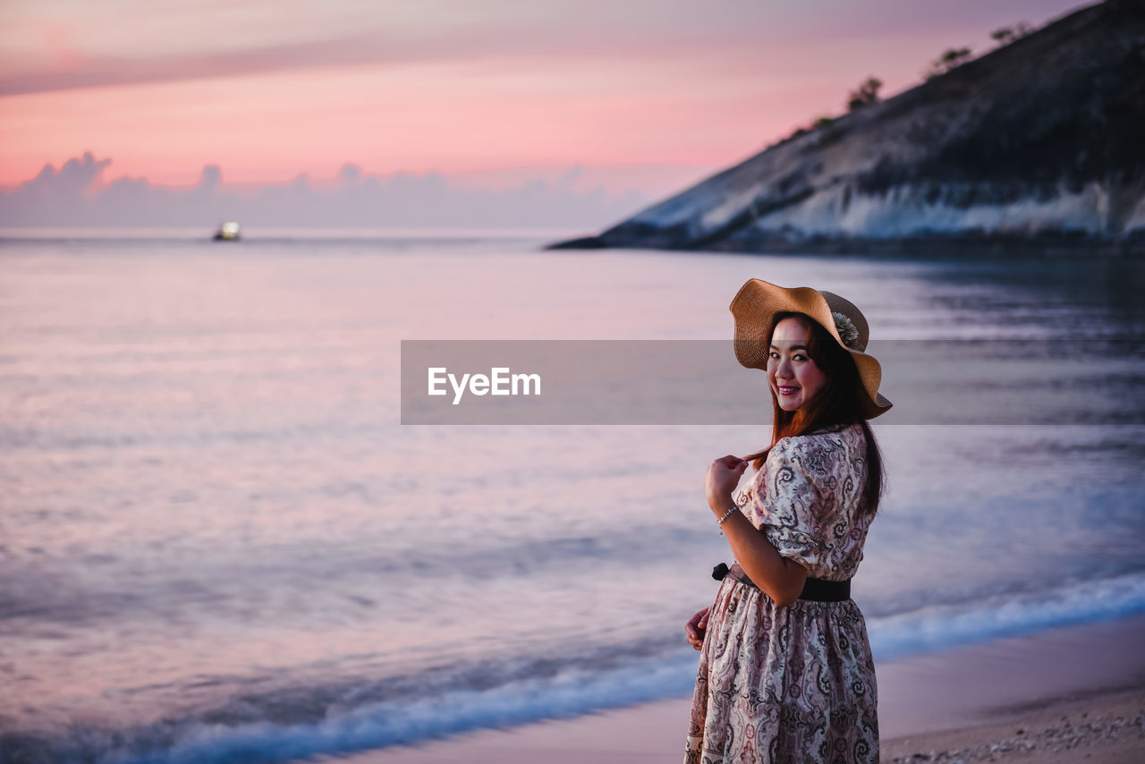 WOMAN STANDING AT BEACH AGAINST SKY