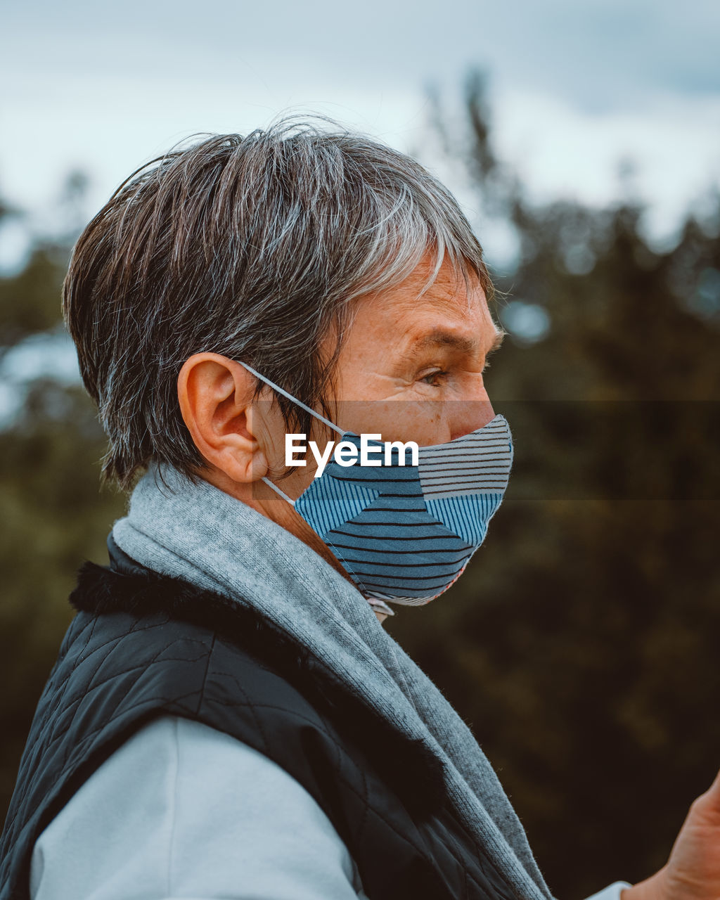 Portrait of an elder woman wearing surgical mask on nature background.