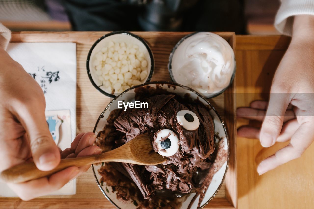 Cropped hand of person holding wooden spoon over chocolate dessert in bowl on table