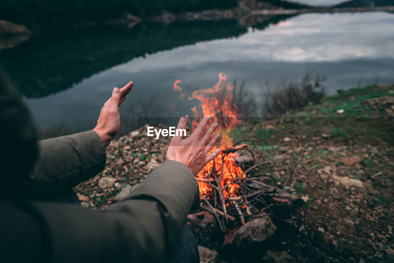 Midsection of woman by fire and lake against sky