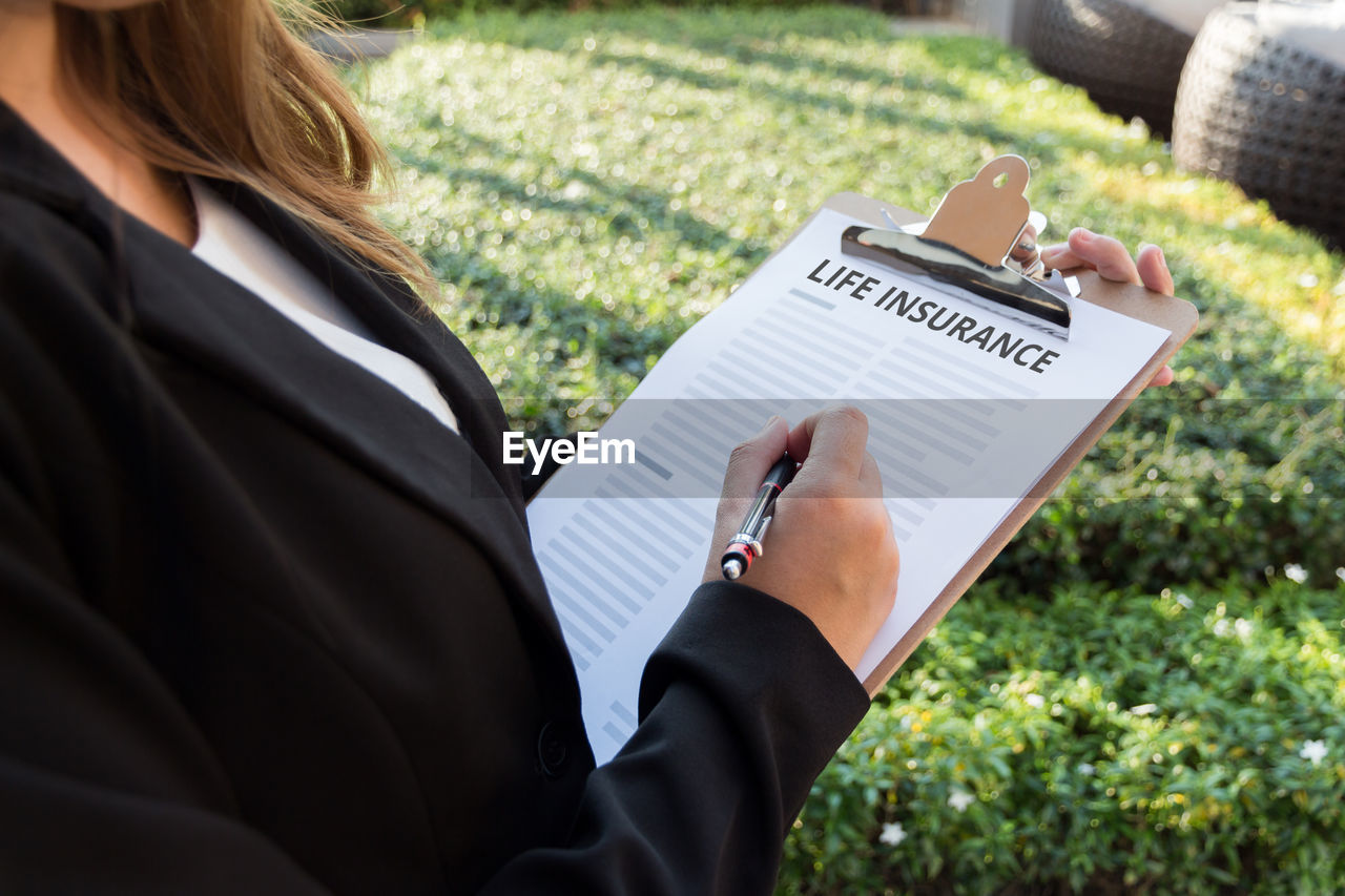 Midsection of female agent with life insurance documents in yard