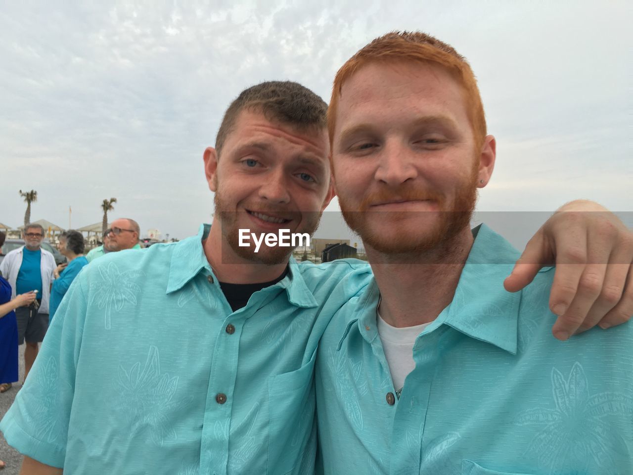 Smiling friends wearing blue shirt standing against sky