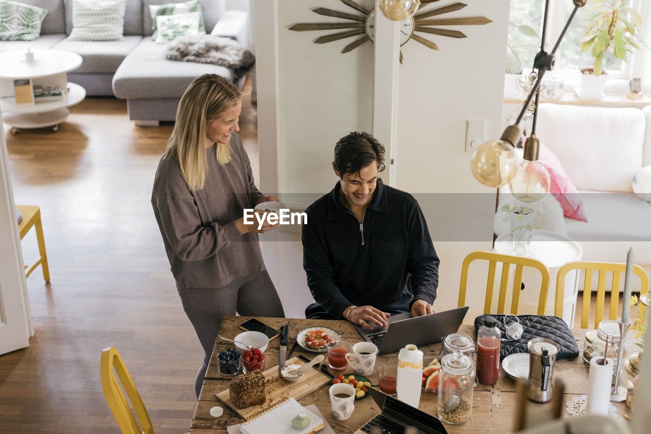 High angle view of happy couple having breakfast while working at home