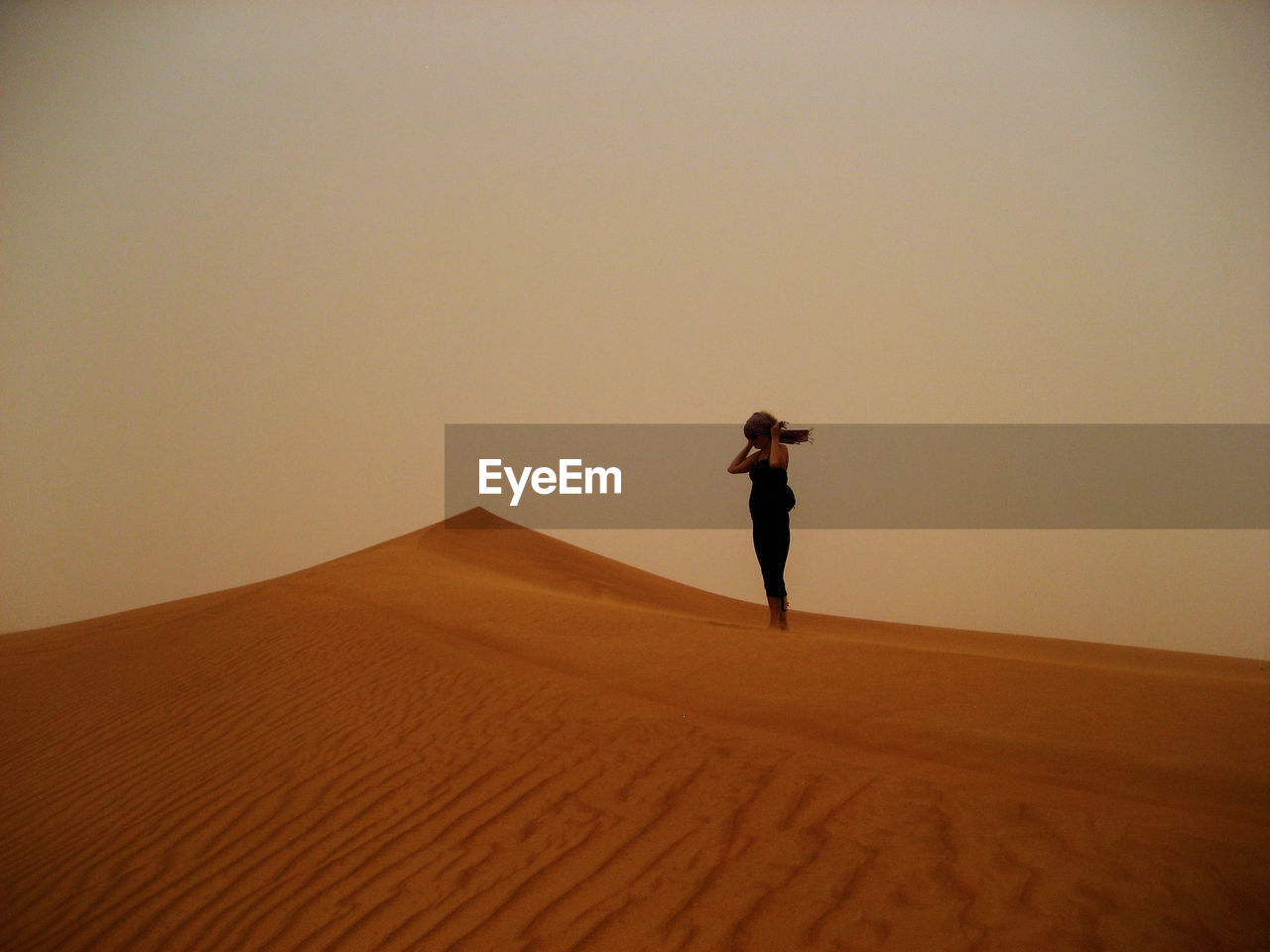 Woman standing on sandy desert against clear sky during sunset