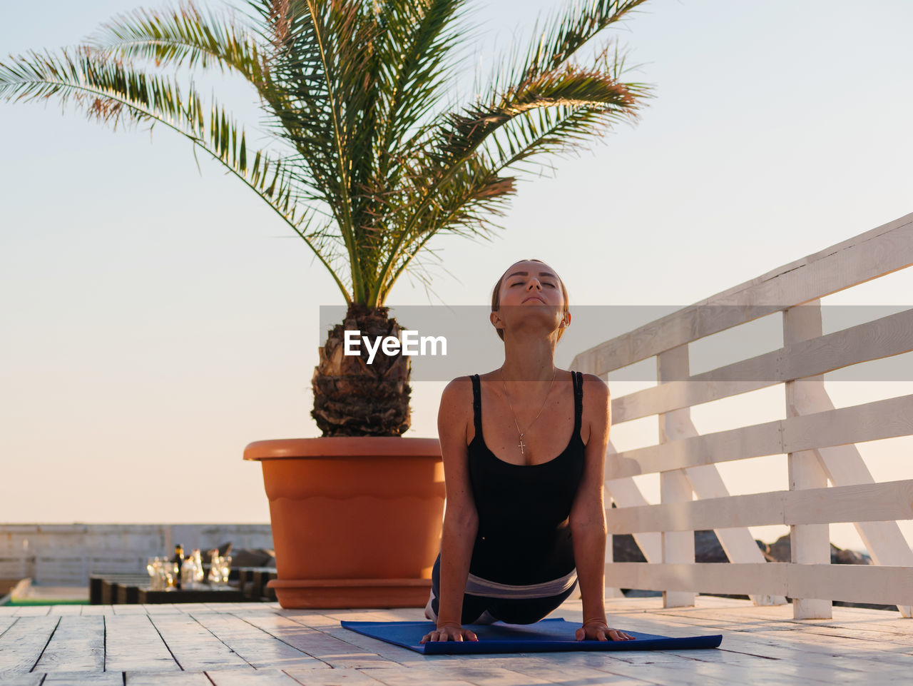 Woman with closed eyes doing yoga on promenade against clear sky during sunrise