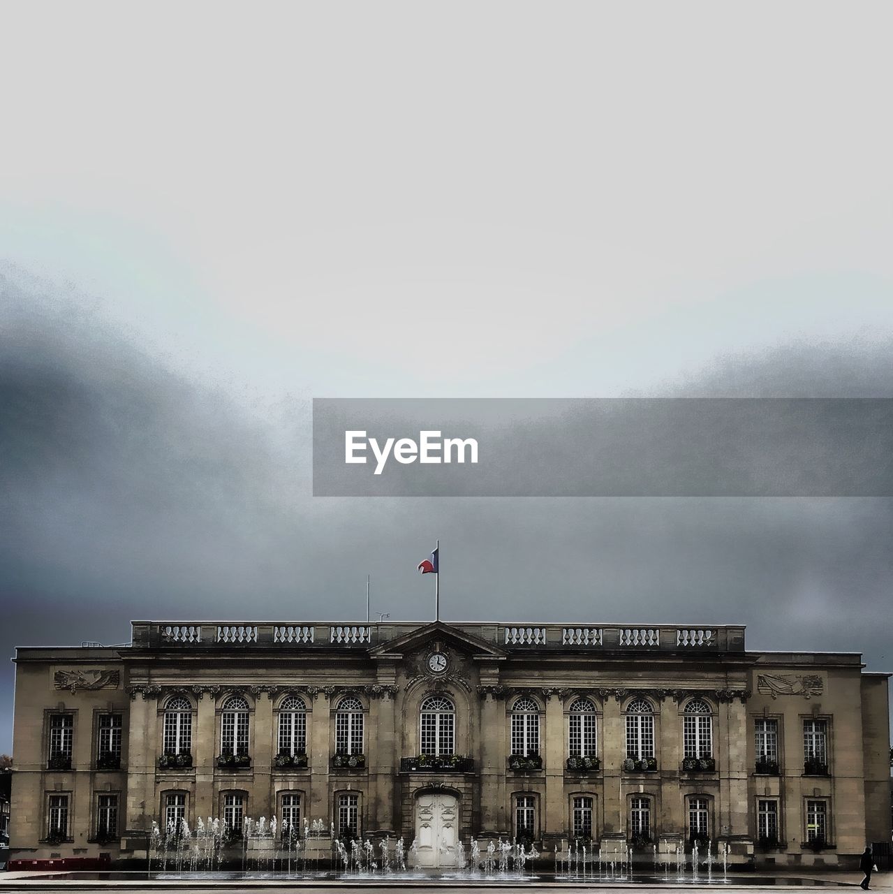 Facade of city hall with fountain against cloudy sky