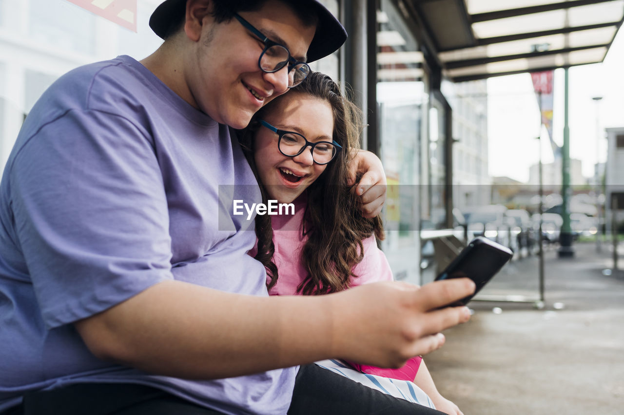 Smiling brother sharing smart phone with sister at bus station