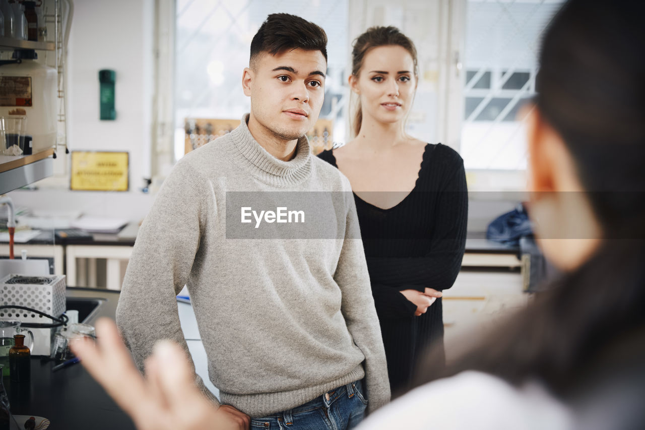 Young chemistry students looking at female teacher in laboratory