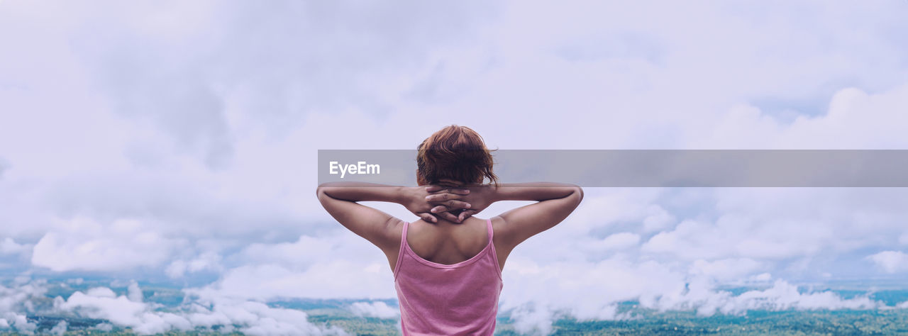 low angle view of woman with arms raised standing against sky