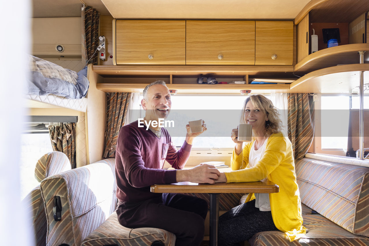Happy mature couple having coffee in camper van