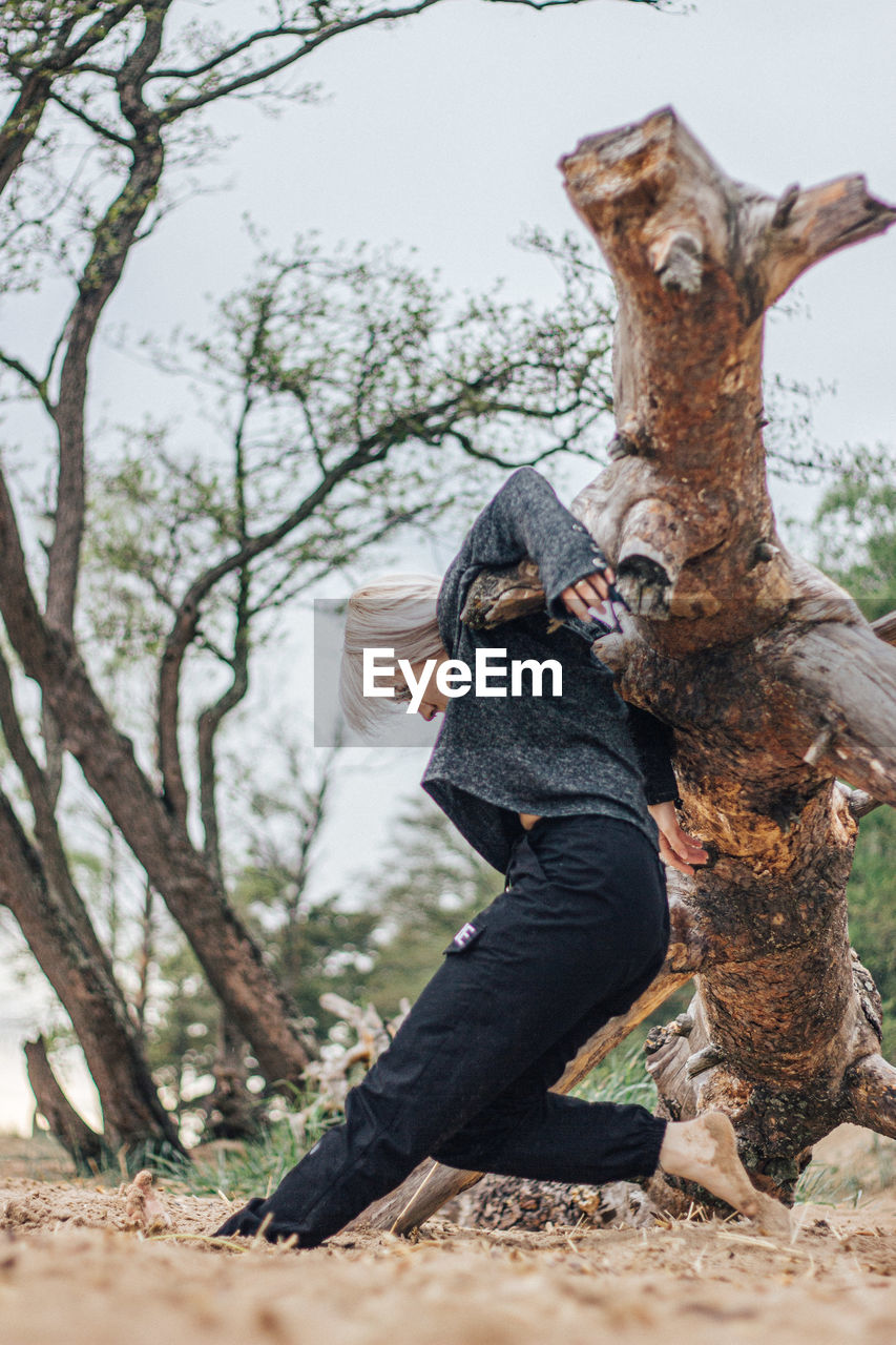 Full length of woman standing on fallen tree at forest