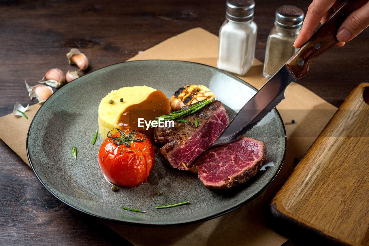 Filet mignon with mashed potatoes and grilled tomato and garlic on a plate with rosemary