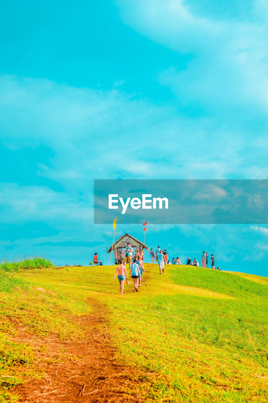 People on grassy field against cloudy sky