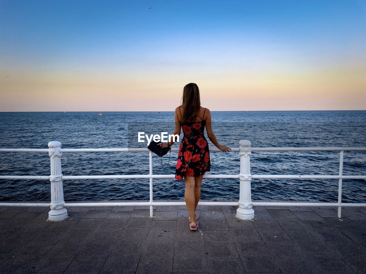 Rear view of woman wearing summer dress looking at the ocean at sunset