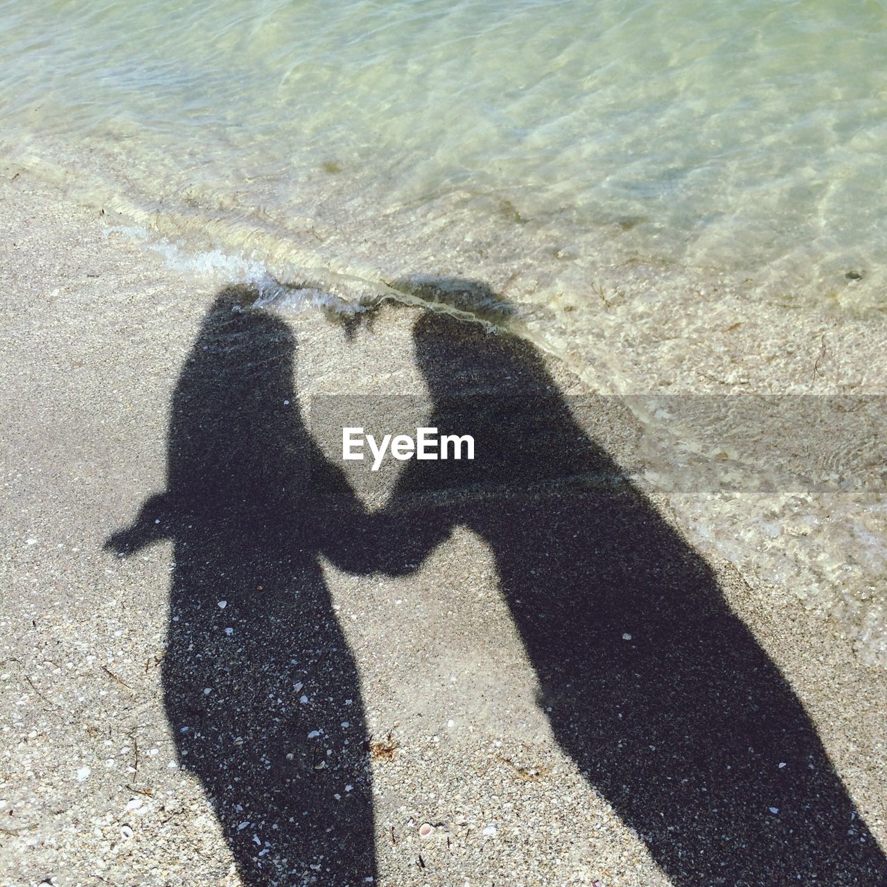 High angle view of friends shadow forming heart on sea shore