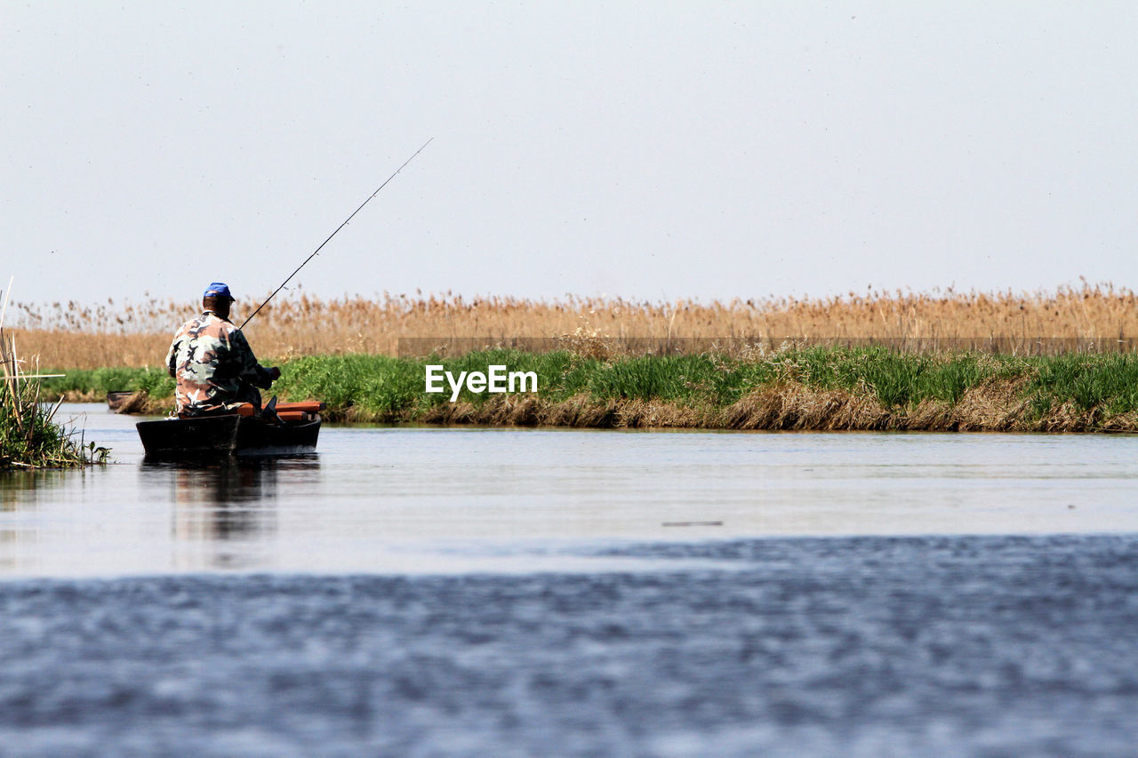 Rear view of man boat fishing in lake during sunny day