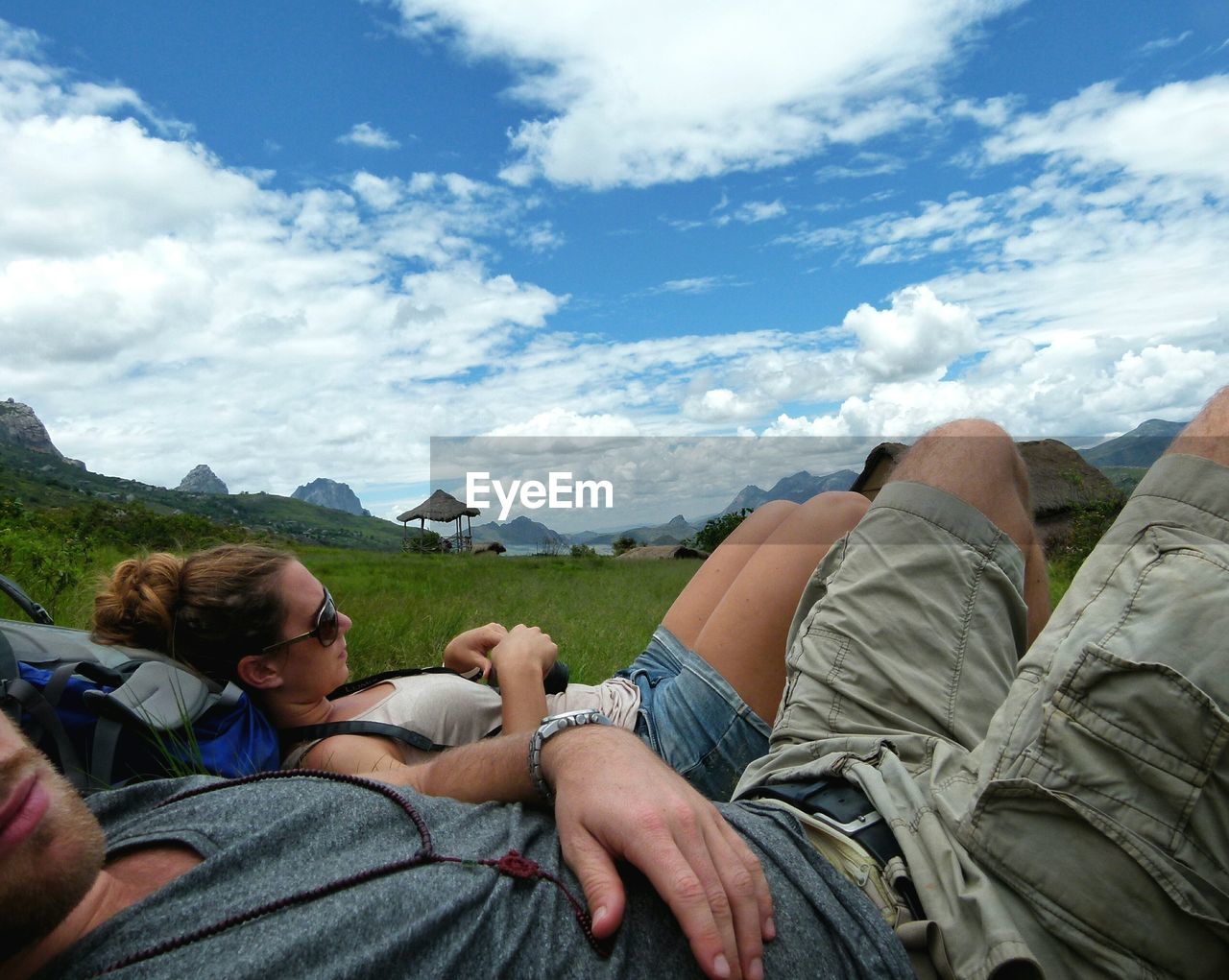 Male and female hikers relaxing on field against sky