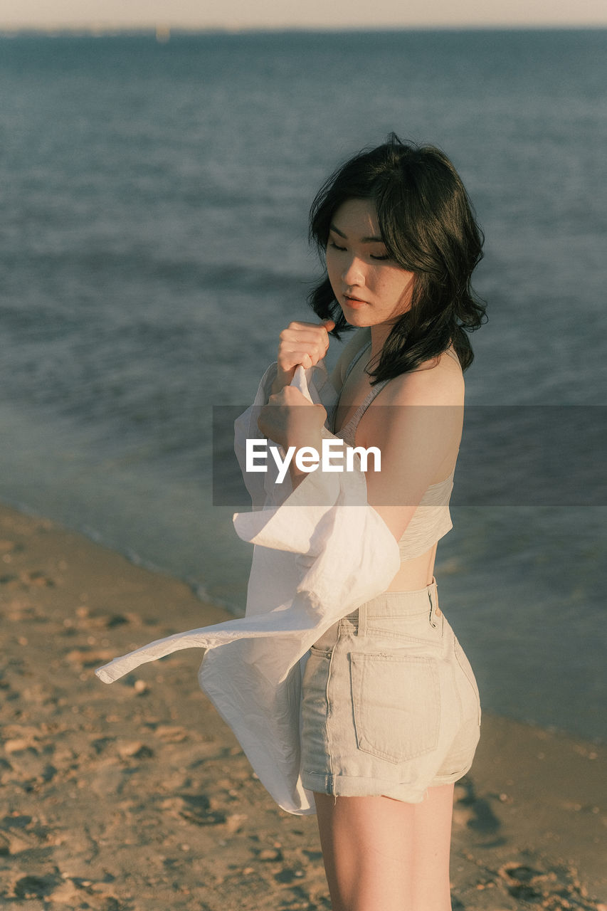 Young woman standing at beach during sunset, with white blouse