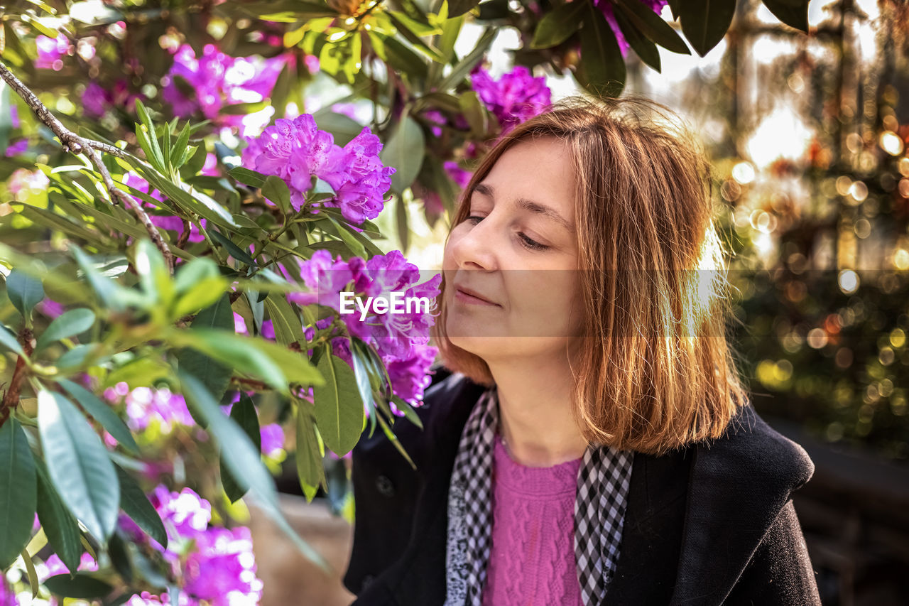 Portrait of a young happy woman with red hair. a blooming spring garden. pink rhododendron flowers.