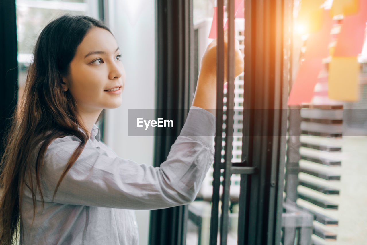 Young businesswoman sticking adhesive note on window at office